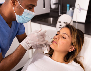 Young Hispanic woman getting procedure of injection contouring for facial correction in aesthetic...