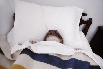 Boy hiding in bed under the covers