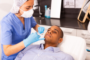 Fototapeta premium Latin american man getting injections for face skin tightening at aesthetic cosmetology clinic