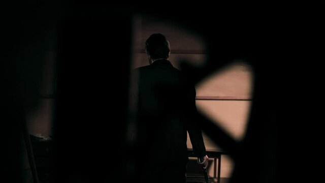 Mysterious back of man in black suit standing alone in dark room. Rack focus
