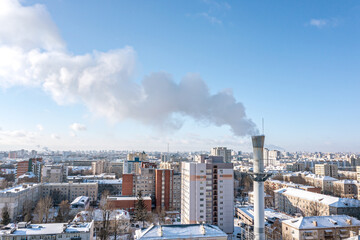 Obraz premium smoking pipe of thermal power plant against blue sky and cityscape in winter time. aerial photography.