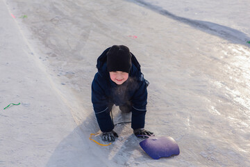 Fototapeta na wymiar Little boy sledding on a snow slide