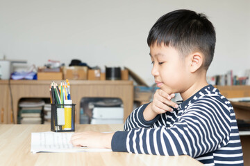 Asian boy who are studying in elementary school reading and doing homework by himself at home.