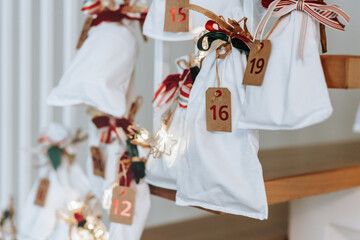 Advent calendar. White surprise bags decorated with colorful red-green Christmas ribbons. Advent calendar ideas for kids.