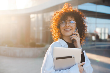 Close up portrait of a curly-haired businesswoman walking outdoor holding a laptop computer and...