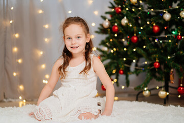 happy little girl in white dress at the Christmas tree. Happy New Year. fashionable elegant clothes for girls.