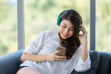 Close up shot portrait of young beautiful Asian woman sitting on sofa  and listening to music with...