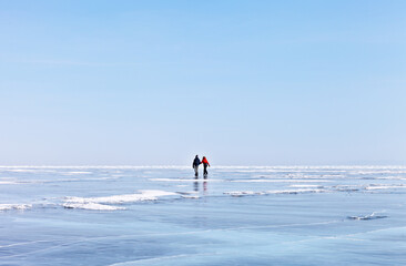 People go ice skating on frozen Lake Baikal on a sunny winter day. Couple of young people actively resting outdoors on a weekend. Natural winter blue background. Active recreation concept
