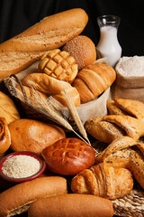Close up of bread basket in wooden background and table with milk, eggs, flour and ears of wheat. Food and bakery concept. Vertical photo.