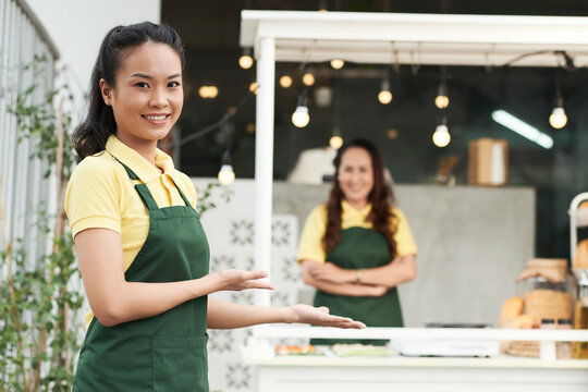 Portrait of smiling young woman welcoming customers to buy sandwich at street food cart