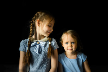 Portrait of two sisters on a dark background. Family taking. One sister looks at the other. Front...