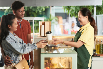 Happy diverse young couple buying coffee in local cafe