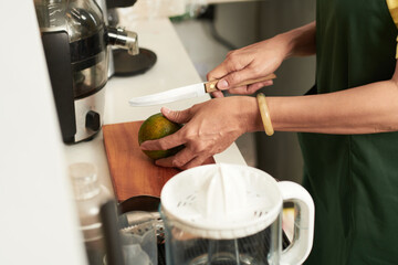 Close-up image of female cafe worker cutting green peel oranges for making juice
