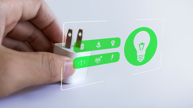 Hand holding the power plug and there is a green power icon on the screen. Energy-saving concept for the environment