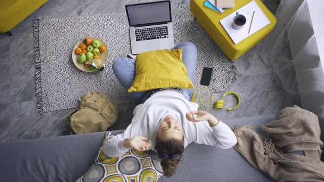 Woman working on floor with laptop on knees in modern apart. She taking break leaning on couch after long sedentary computer work, stretching tense muscles after studying in incorrect posture 