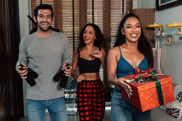 Group of cheerful and fun male and female friends with beer bottles gifts arriving at home for a beautiful housewarming party during christmas