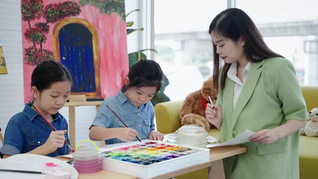 In an art school, a beautiful Asian teacher is teaching children in a painting class, the concept of education.
