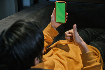 An Asian guy lays on sofa in office, communicates by mobile phone