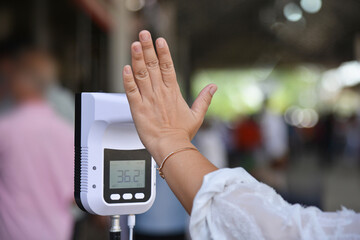 Close-up Woman hand with Touchless infrared thermometer with blurred people background.