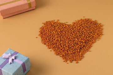 Heart shape with boxes of gifts on an orange background. The figurine is made of bright orange shiny beads. Valentine's day signs and symbols for copy space. Festive mockup.	