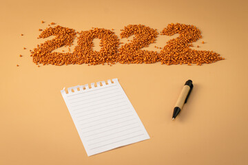 The number 2022 next to a notebook and a planning pen. The figure is made of bright orange shiny beads. Signs and symbols of the new year for copy space. Festive mockup.