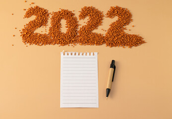The number 2022 next to a notebook and a planning pen. The figure is made of bright orange shiny beads. Signs and symbols of the new year for copy space. Festive mockup.