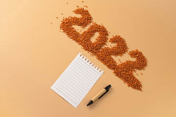 The number 2022 next to a notebook and a planning pen. The figure is made of bright orange shiny beads. Signs and symbols of the new year for copy space. Festive mockup.