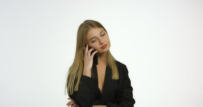 Beautiful woman with long blond hair in a black jacket dials a phone number and waits for an answer. Girl model posing in the studio at the camera in the studio on a white background.