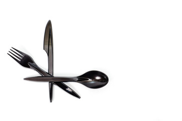 A set of plastic cutlery knife, fork and spoon in black, filmed on a white background