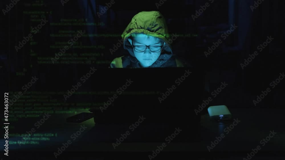 Poster young boy hacker typing on laptop with security codes moving in the screen in a dark workplace. - st