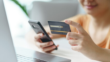 Young woman holding credit card and using smartphone for online shopping, internet banking, e-commerce, spending money, working from home concept