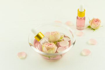 glass bowl with rose water, flowers and rose petals, cosmetic bottles with zfir flower oil. aromatherapy, anti-stress.