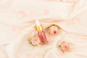 natural cosmetic product. rose petal oil in a glass flamon with a dropper on a pastel textile background with rose buds.