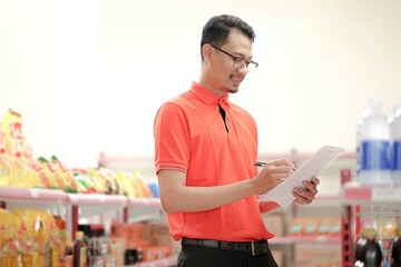  supervisor making notes to the clipboard while standing near a rack of mixed goods.