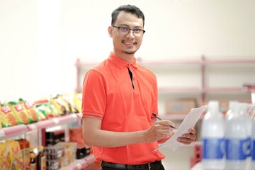 Smiling  supervisor making notes to the clipboard while standing near a rack of mixed goods.