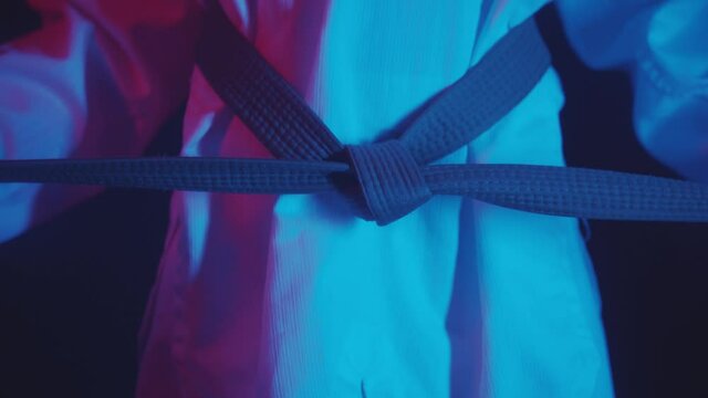A little boy doing taekwondo in neon lighting - tying up the belt and showing moves with his hands