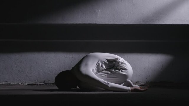 Mad man in white clothes lying in fetal position and getting up