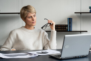 Portrait of a mature businesswoman working at a laptop in the workplace in the office, takes off her glasses and thinks while looking at the laptop