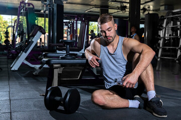 Athletic young man  relax and drink water after dumbbell work out or exercise in fitness gym. Bodybuilding and healthy lifestyle concept.