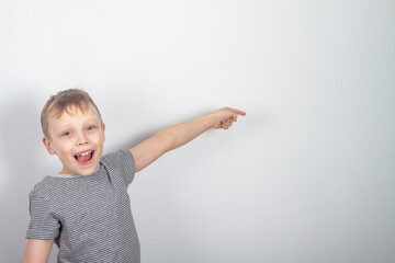 Cheerful caucasian boy smiles and points with his finger on a gray background