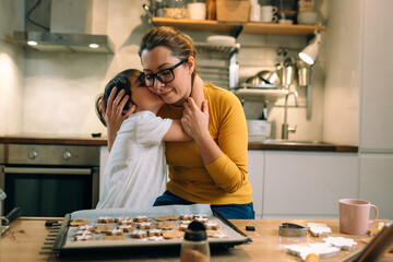 mother and child in kitchen, preparing cookies. child kissing his mother