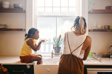 Young girl blowing soap bubbles at her mom in the kitchen - Powered by Adobe