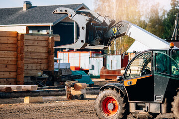 Loader carries logs against background of building wooden house