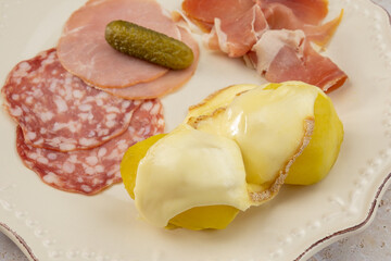 fromage à raclette fondu sur des pommes de terre et charcuterie dans une assiette