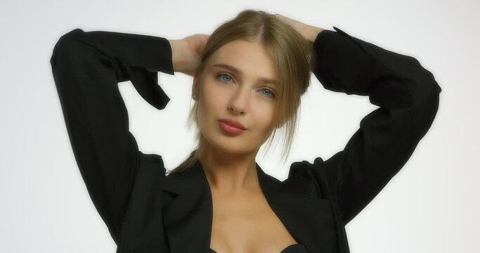 Beautiful girl in a black shirt collects her hair and blows a kiss. Young Caucasian woman poses for the camera in a studio on a white background. Portrait of a beautiful female face.