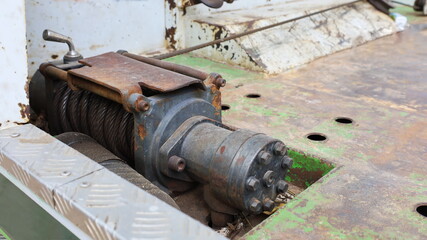 Fototapeta na wymiar Rusty old electric winch. Close-up of a used grunge pulley and electric motor with rolled steel wires on a metal floor of a slide with copy space. Selective focus