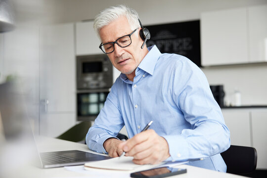 Male Professional With Wireless Headset Writing In Book At Office