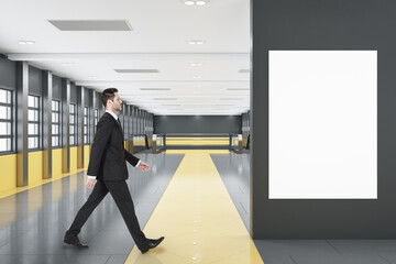 Fototapeta premium Businessman walking in modern black and orange tile shopping mall or airport interior with empty white mock up poster on wall, windows, city view and escalator. Public area concept.