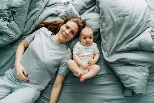 Top View Of A Caring Mommy With A Baby On The Bed In The Bedroom.