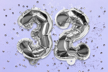 Silver foil balloon number, digit thirty two on a lilac background with sequins. Birthday greeting...